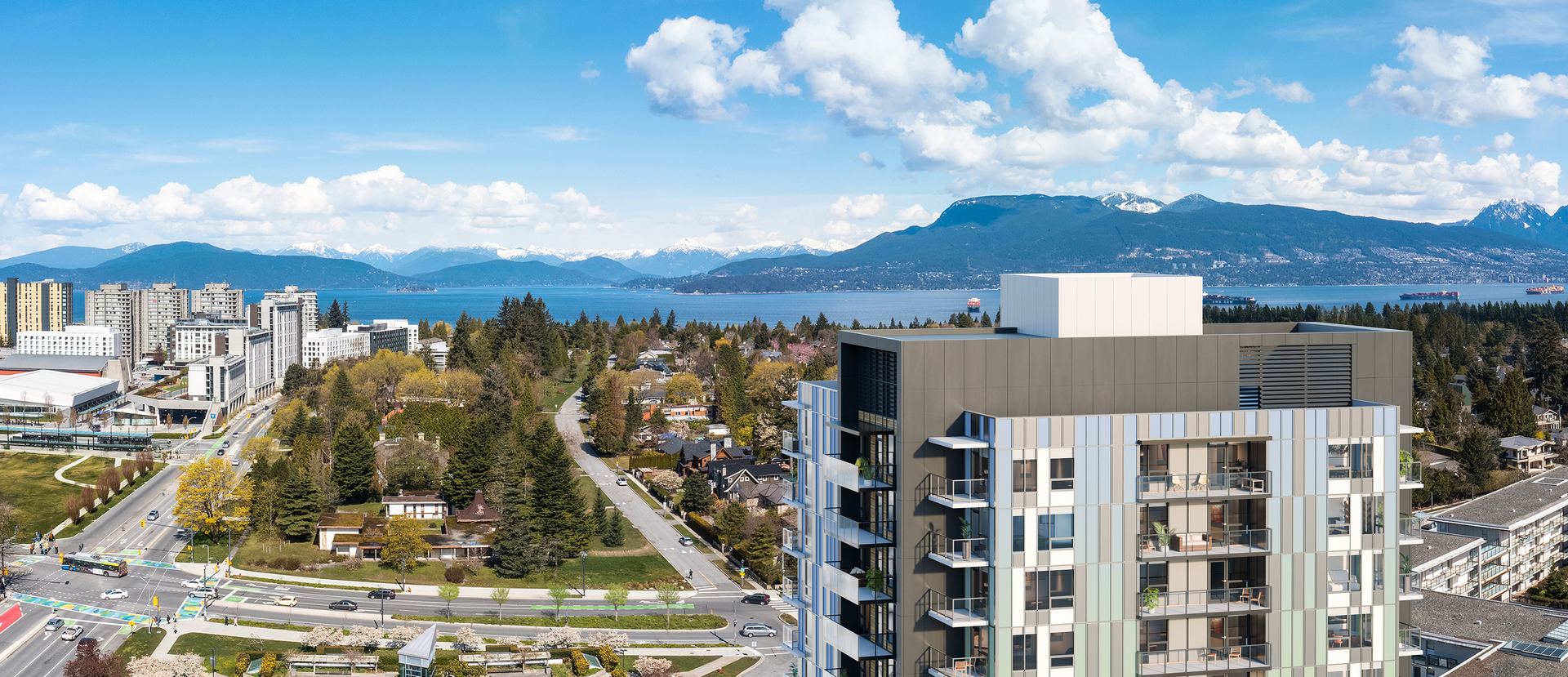 Aerial view from the building over the UBC campus and treetops, with the water and snow-capped mountains on the horizon.